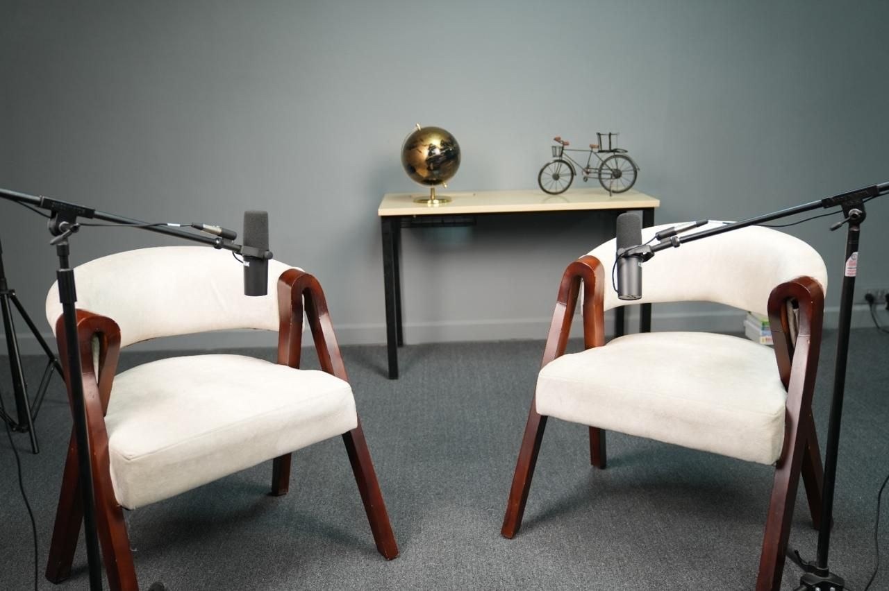 Podcast set with two white upholstered chairs and boom mics