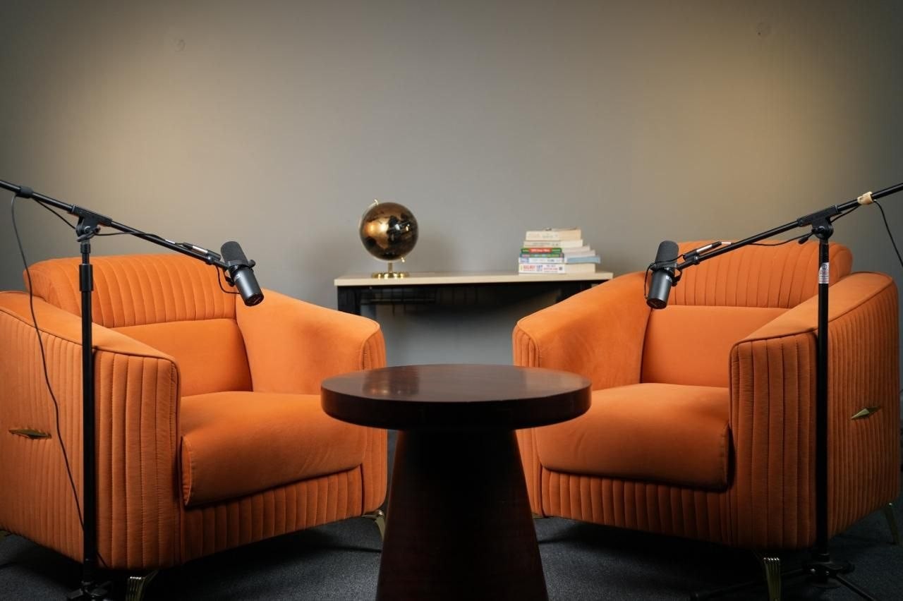 Podcast set with two orange armchairs, boom mics and a round wooden table